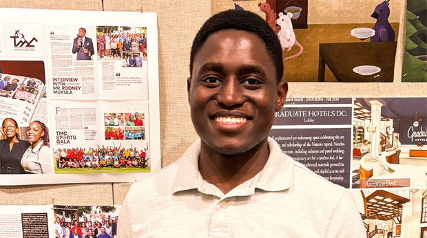 La Roche University alumnus Edwin Kavuma smiling, standing in front of a display board featuring various posters and photographs